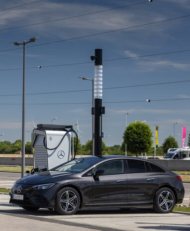 Mercedes-Benz an einer Ladestation mit Windrädern im Hintergrund.