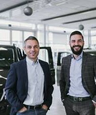 Zwei Männer in einem Mercedes-Benz Autohaus mit Vans im Hintergrund.