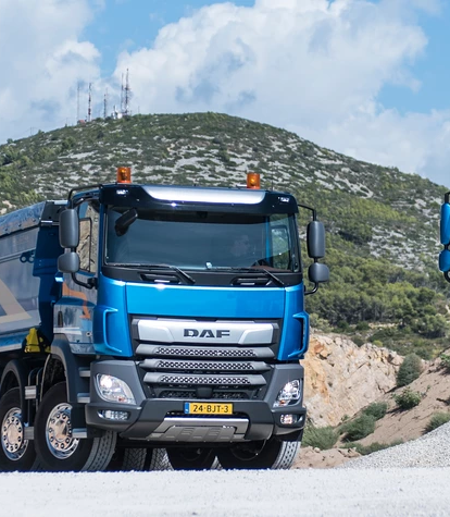 Drei blaue DAF-Lkw parken in einer Steinbruchlandschaft.