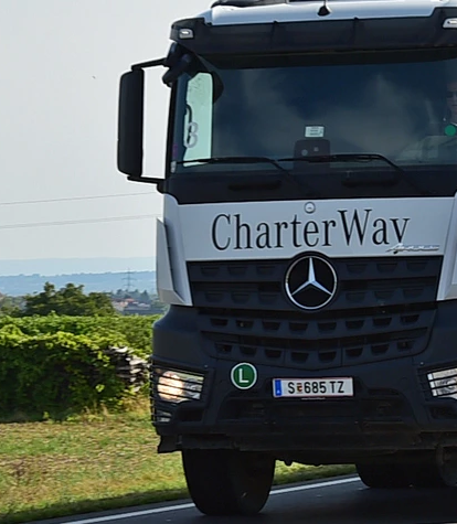 Ein Mercedes-Benz Lastwagen fährt auf einer Landstraße entlang, umgeben von Bäumen und einer Wiese.