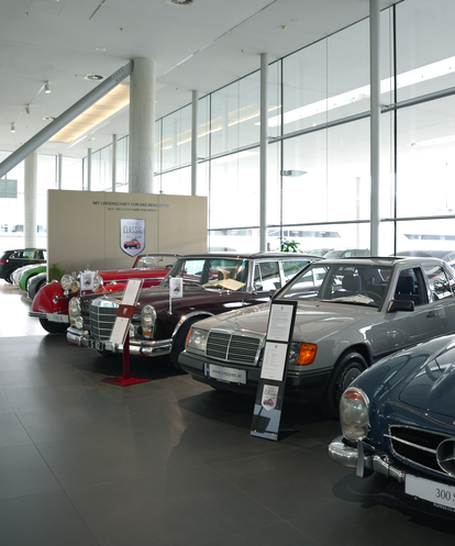 Ein Showroom mit klassischen Mercedes-Benz Modellen, darunter ein 300 SL. Verschiedene Fahrzeuge nebeneinander ausgestellt.