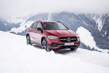 Ein roter Mercedes-Benz GLA auf einer verschneiten Straße mit Bergkulisse.