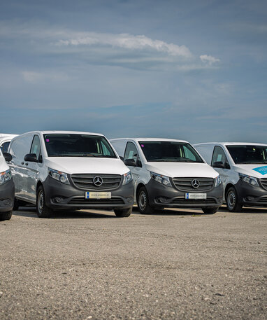 Mehrere weiße Mercedes-Benz Transporter parken in einer Reihe.