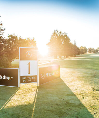 Golfplatz mit Mercedes-Benz-Banner bei Sonnenaufgang, Startpunkt Loch 1.