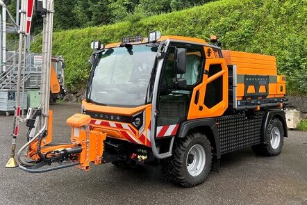 Ein HANSA APZ 1003 XL mit  Gießanlage der Firma Fiedler, der auf einer Straße geparkt ist, umgeben von Bäumen und Sträuchern.