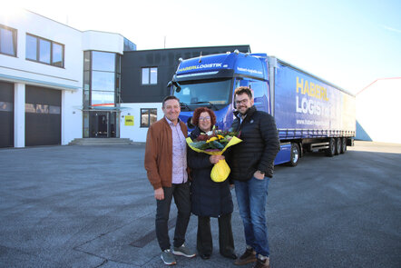 Zwei Männer und eine Frau mit Blumenstrauß vor einem blauen Haberl Logistik-Lkw.
