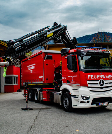 Feuerwehrfahrzeug mit Kranarm vor einer Feuerwache in bergiger Kulisse. | © Rene Oberhuemer