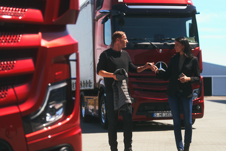 Zwei Personen unterhalten sich vor roten Mercedes-Benz Actros L.