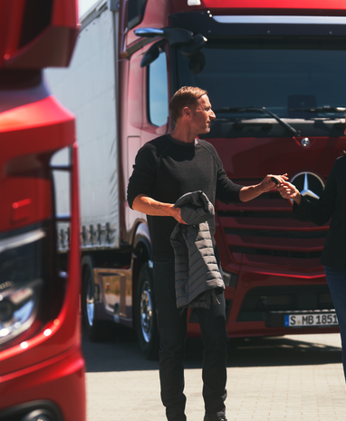 Zwei Personen unterhalten sich vor roten Mercedes-Benz Actros L.