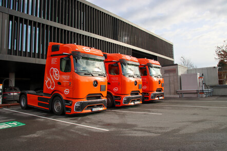 Drei orange Mercedes-Benz eActros, die an Ladestationen parken. | © Daimler Truck Austria