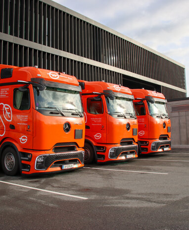 Drei orange Mercedes-Benz eActros, die an Ladestationen parken. | © Daimler Truck Austria