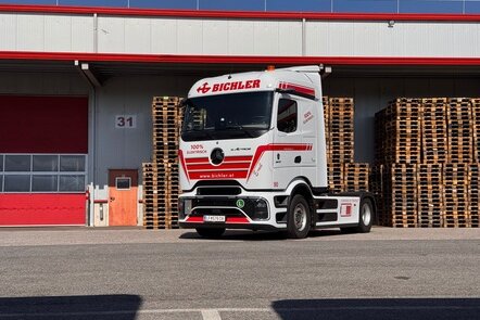 Ein weiß-roter Mercedes-Benz eActros mit Bichler-Logo vor einem Lagerhaus.