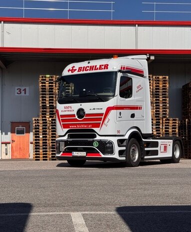 Ein weiß-roter Mercedes-Benz eActros mit Bichler-Logo vor einem Lagerhaus.