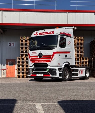Ein weiß-roter Mercedes-Benz eActros mit Bichler-Logo vor einem Lagerhaus.