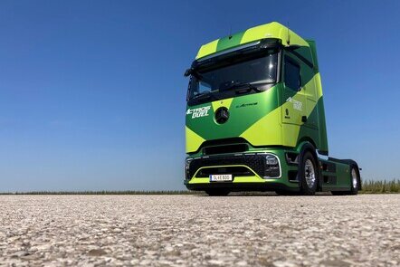 Ein grüner Mercedes-Benz eActros auf einer asphaltierten Fläche unter blauem Himmel.