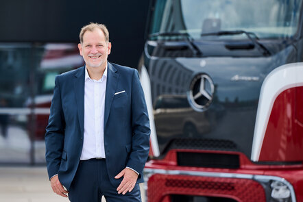 Bernhard Rusch steht im Anzug lächelnd vor einem Mercedes-Benz Lkw.