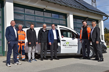 Personen vor einem Fahrzeug der Gemeinde Wals-Siezenheim, einer trägt eine orange Arbeitskleidung.