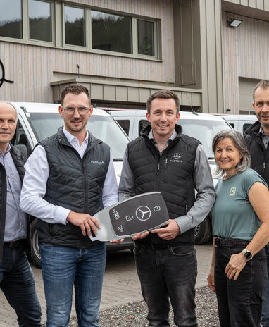Fünf Personen bei der Übergabe eines großen Mercedes-Benz Schlüssels vor mehreren Transportern. | © Lorenz Masser