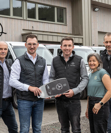 Fünf Personen bei der Übergabe eines großen Mercedes-Benz Schlüssels vor mehreren Transportern. | © Lorenz Masser