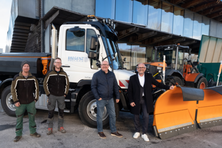 Vier Männer stehen vor einem weißen Unimog mit Schneepflug, bereit für den Winterdienst.