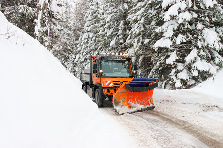 Ein orangefarbener Schneepflug räumt eine schneebedeckte Straße frei.