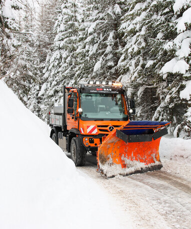Ein orangefarbener Schneepflug räumt eine schneebedeckte Straße frei.
