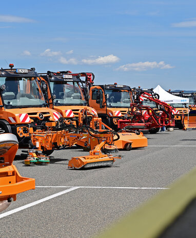Mehrere orangefarbene Spezialfahrzeuge und Maschinen bei einer Ausstellung aufgereiht.