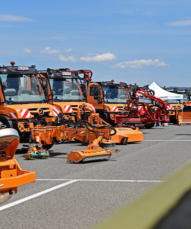 Mehrere orangefarbene Spezialfahrzeuge und Maschinen bei einer Ausstellung aufgereiht.