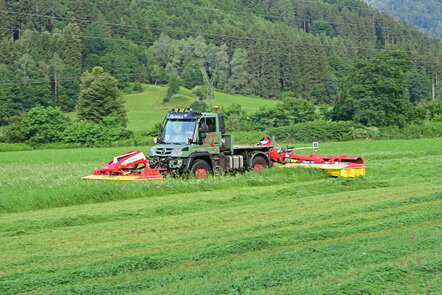 Ein Mercedes-Benz Unimog mit einem Mähwerk im Einsatz auf einem Feld.