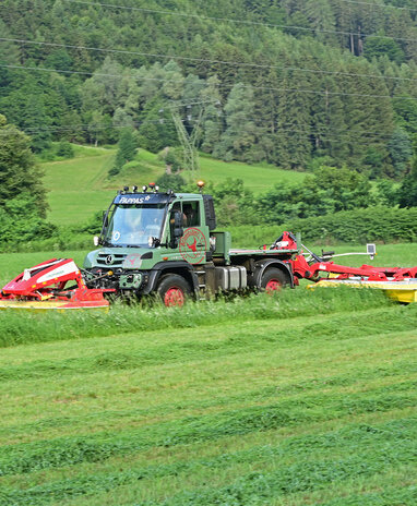 Ein Mercedes-Benz Unimog mit einem Mähwerk im Einsatz auf einem Feld.