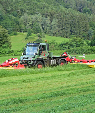 Ein Mercedes-Benz Unimog mit einem Mähwerk im Einsatz auf einem Feld.