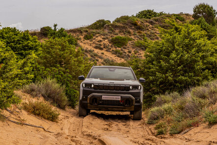 Ein Jeep Compass 4xe fährt durch eine sandige, bewachsene Landschaft.