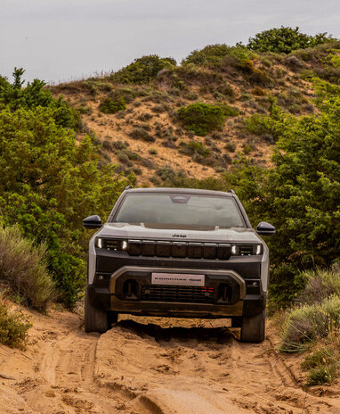 Ein Jeep Compass 4xe fährt durch eine sandige, bewachsene Landschaft.