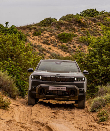 Ein Jeep Compass 4xe fährt durch eine sandige, bewachsene Landschaft.