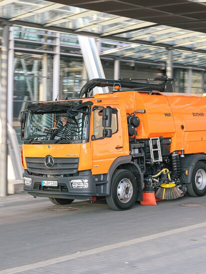 Orangefarbene Mercedes-Benz Kehrmaschine Bucher MaxPowa V65 reinigt die Straße.
