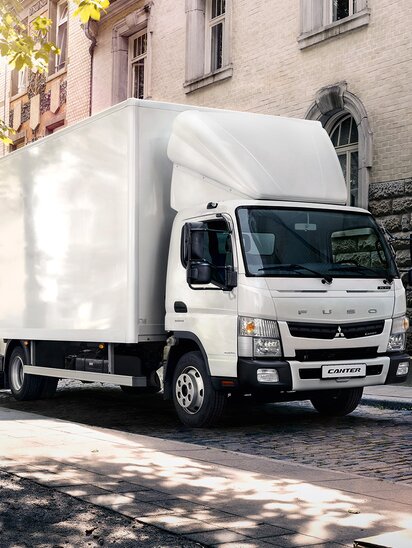 Ein FUSO Canter Lkw transportiert Möbel auf einer Stadtstraße.