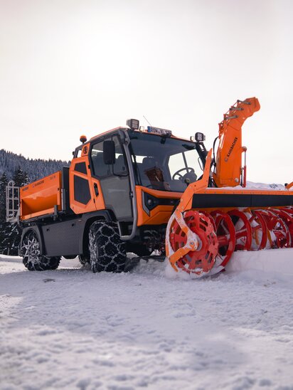 Der Hansa APZ 1003 Mehrzweckgeräteträger räumt Schnee auf einem verschneiten Bergweg.