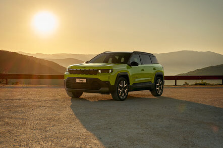 Ein grüner Jeep Compass steht bei Sonnenuntergang in einer Berglandschaft.