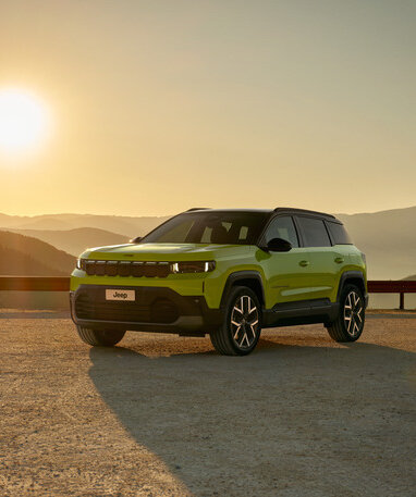 Ein grüner Jeep Compass steht bei Sonnenuntergang in einer Berglandschaft.