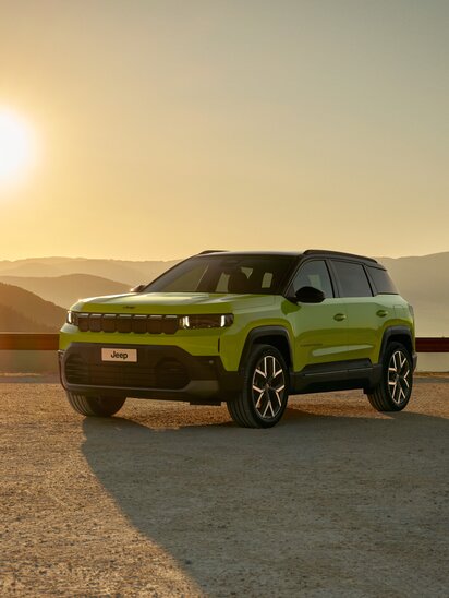Ein grüner Jeep Compass steht bei Sonnenuntergang in einer Berglandschaft.