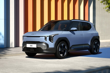 Silberner Kia EV2 SUV bei Sonnenschein vor bunter Streifenwand.