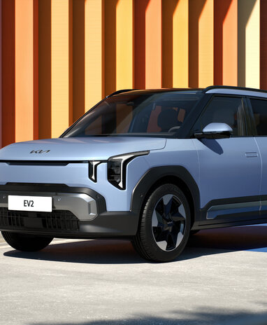 Silberner Kia EV2 SUV bei Sonnenschein vor bunter Streifenwand.