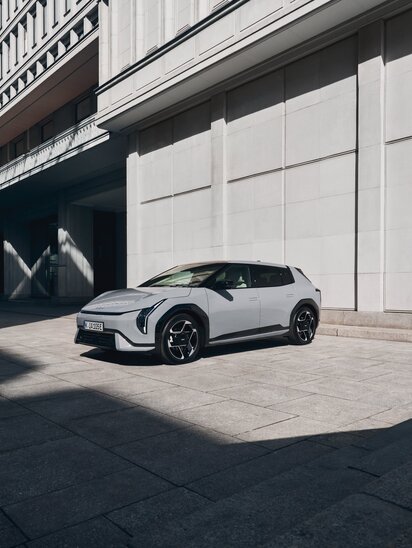 Ein weißer Kia EV4 parkt vor einem modernen Gebäude im Schatten.