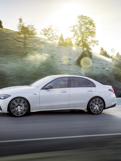 Weiße Mercedes-AMG C-Klasse Limousine fährt auf einer Straße bei Sonnenschein. | © Mercedes-Benz AG