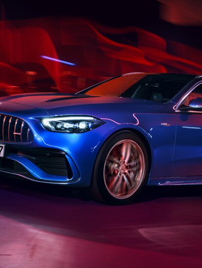Ein blaues Mercedes-AMG C-Klasse T-Modell fährt dynamisch durch eine beleuchtete Kulisse. | © Mercedes-Benz AG