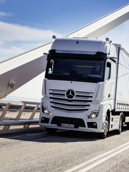 Ein weißer Mercedes-Benz Actros Lkw fährt über eine moderne Brücke.