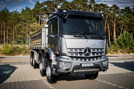 Ein silberner Mercedes-Benz Arocs steht auf einem gepflasterten Platz vor einem Wald.