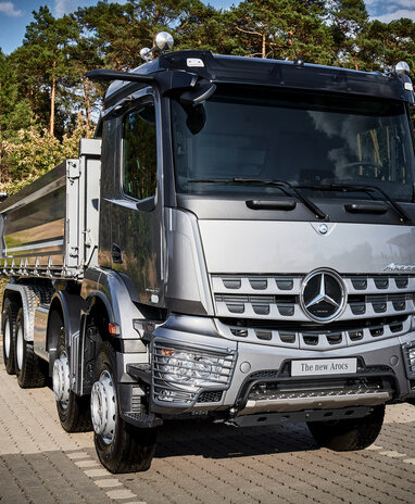 Ein silberner Mercedes-Benz Arocs steht auf einem gepflasterten Platz vor einem Wald.
