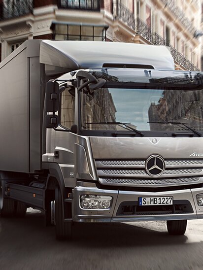 Ein silberner Mercedes-Benz Atego fährt durch eine Stadtstraße.