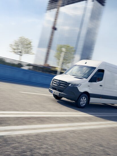 Ein Mercedes-Benz eSprinter Kastenwagen fährt schnell auf der Autobahn vor einem modernen Hochhaus. | © Mercedes-Benz AG